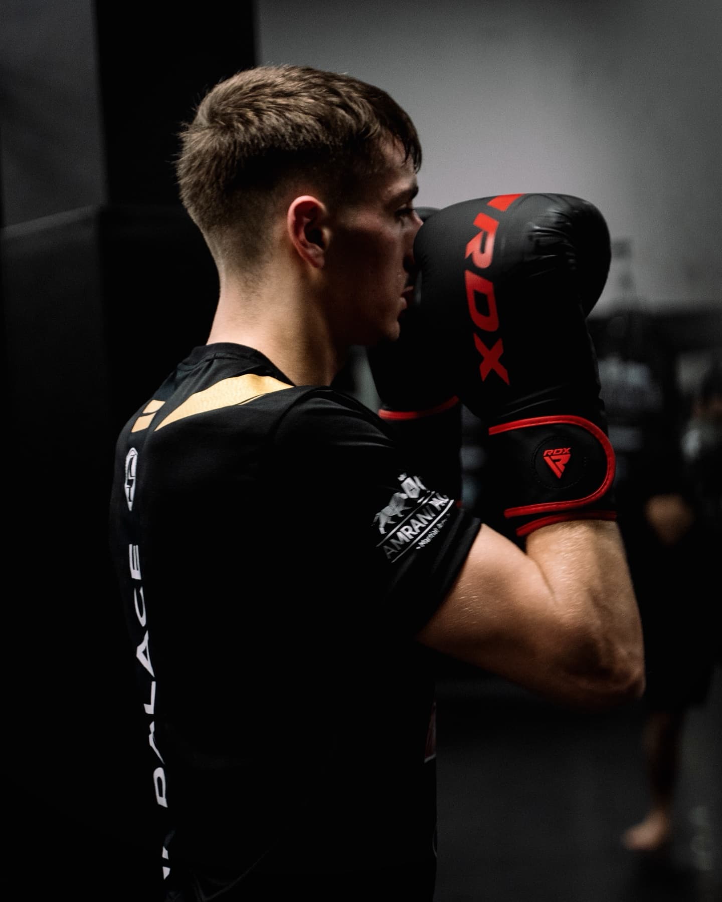 Boxer im Amrani-Palace-Shirt mit rot-schwarzen Boxhandschuhen in hoher Deckung, im Profil beim Training im Amrani Palace Oberhausen